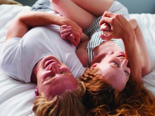 Beautiful man woman couple lying in bed cuddling playful biting together in love lifestyle relationship overhead